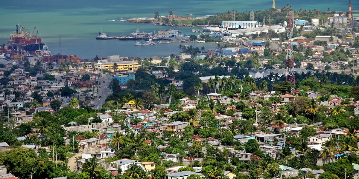 Dominican Republic coastal city with turquoise bay, boats, hillside homes, and lush tropical scenery.